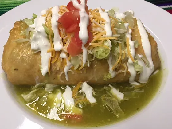 A chimichanga topped with crema, cheese and tomato over salsa verde