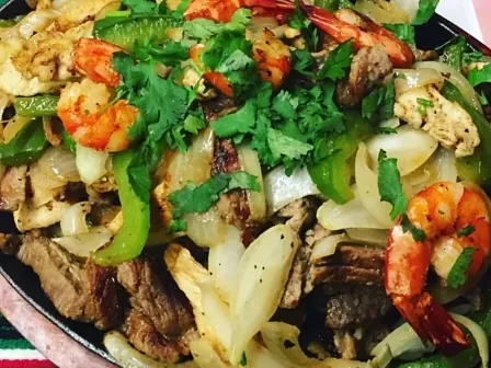A sizzling skillet of mixed fajitas with shrimp, steak, peppers and onion