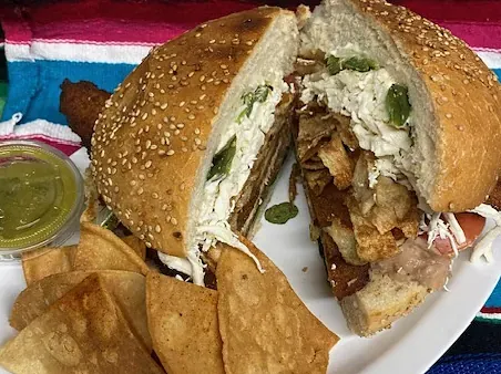 A cemita on a sesame roll, cut in half, with tortilla chips