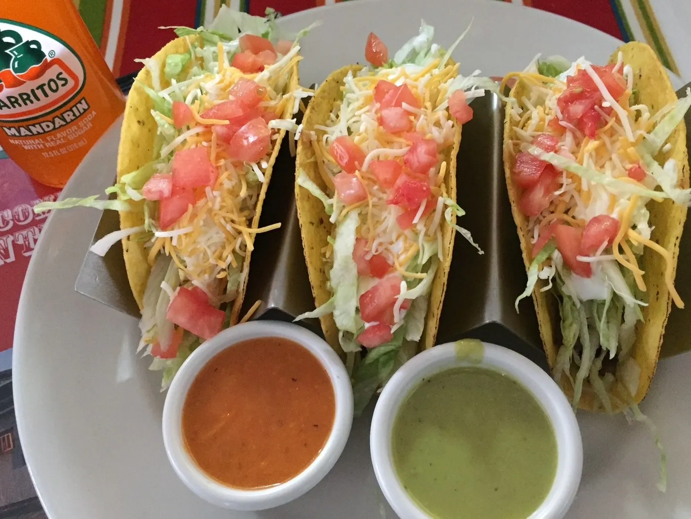 Three hard shell tacos with lettuce, tomato and cheese, and two salsas