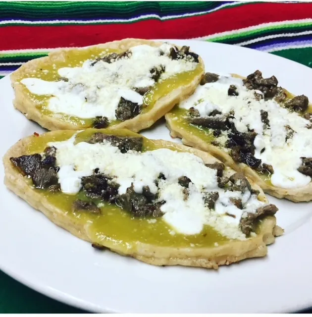 Picaditas topped with green salsa, cream and cheese
